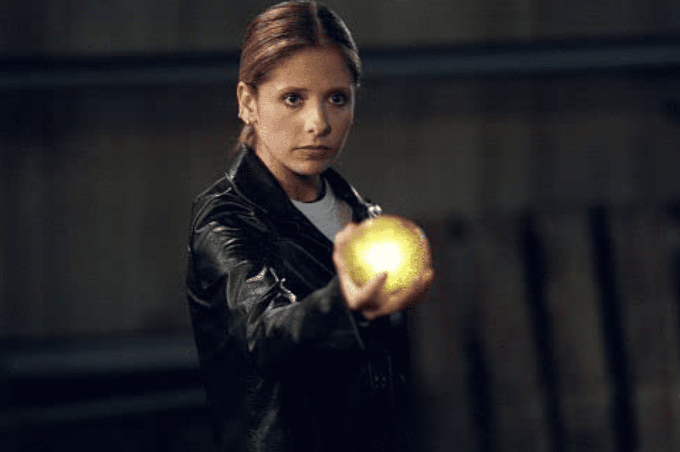 Buffy, wearing a black leather jacket, holds out a glowing, yellow orb