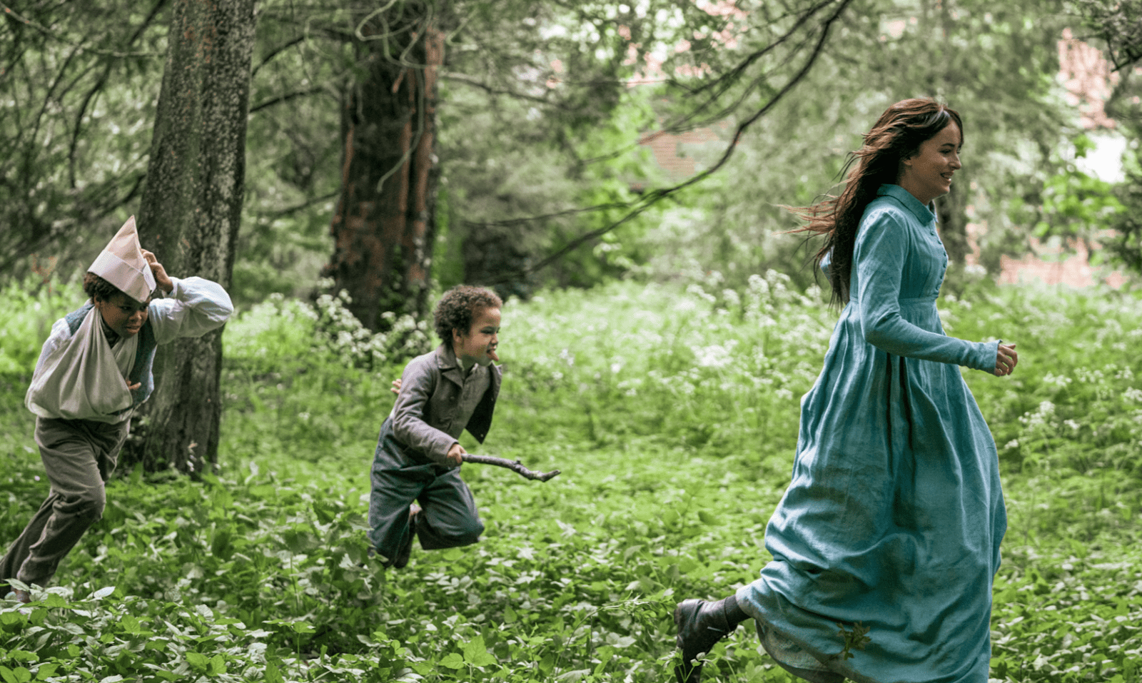 A woman wearing a long, green dress playing with two young kids in a forest