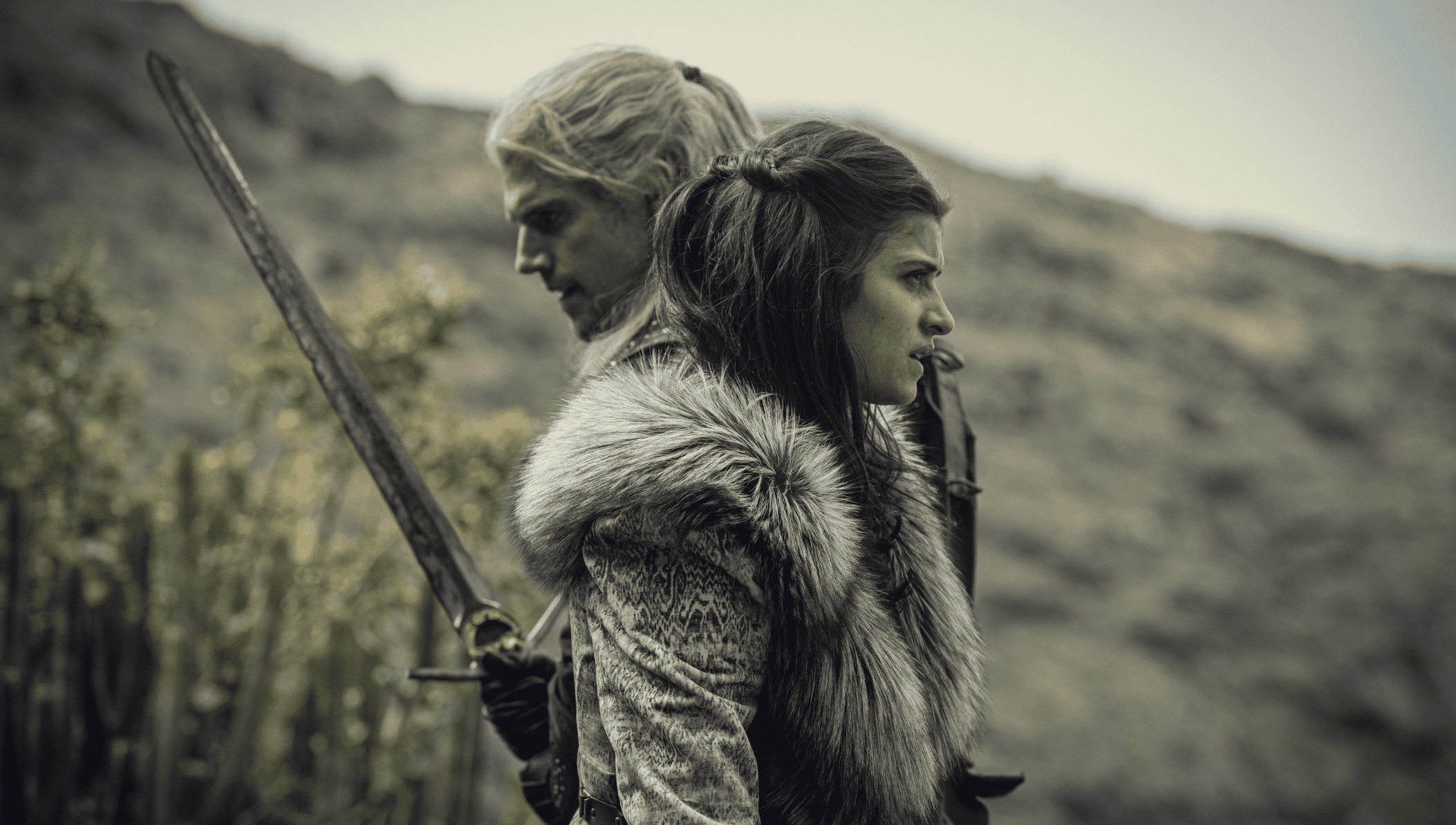 Two of the main characters in “The Witcher,” one holding a sword and the other wearing a fur collar